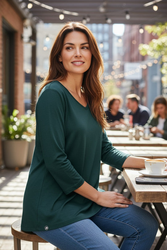 Woman sitting at an outdoor cafe table wearing a green top and blue jeans.