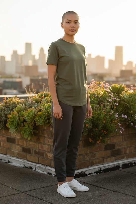 Person wearing a green t-shirt and dark pants standing on a rooftop with a cityscape in the background.