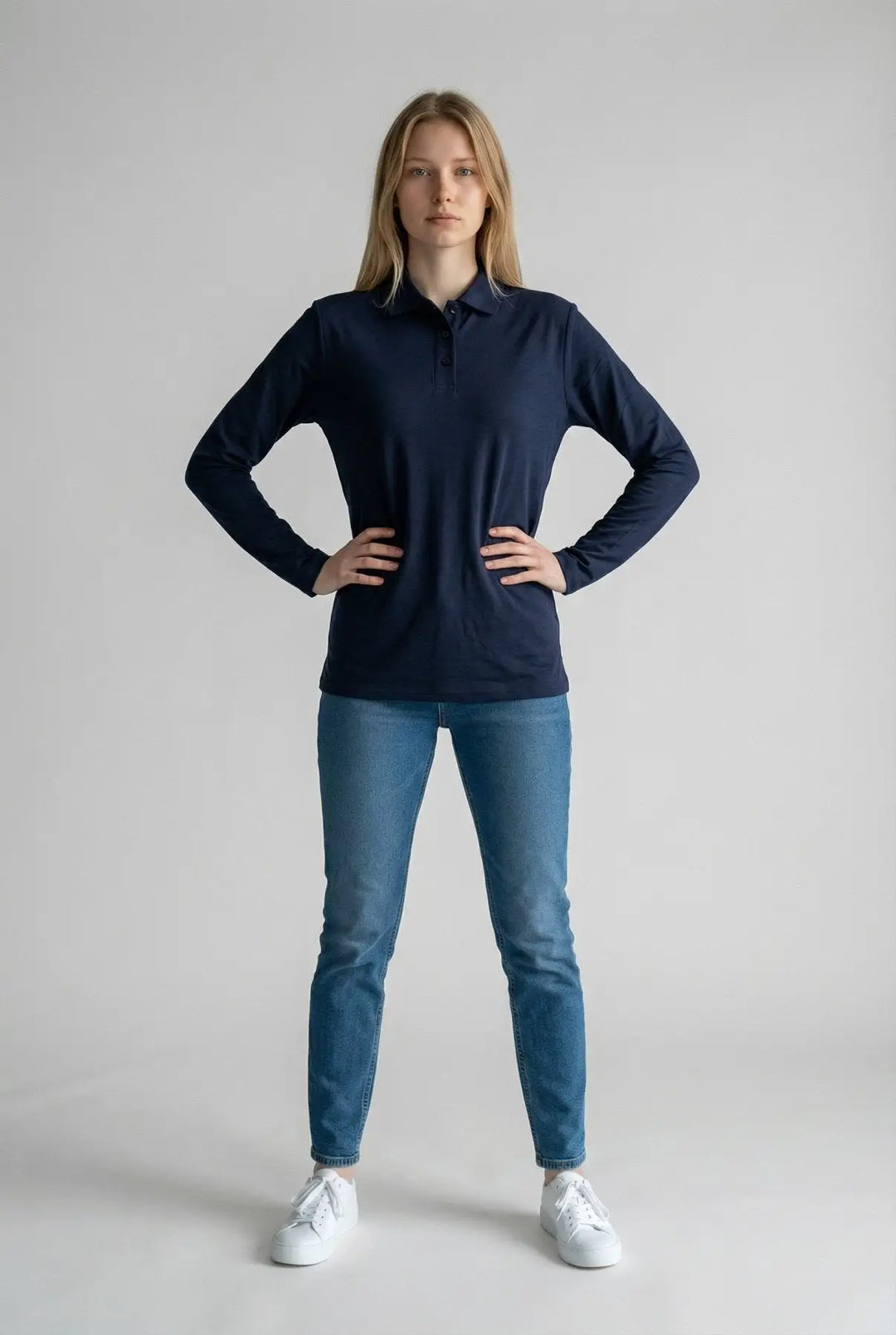 Woman wearing a navy long-sleeve shirt and blue jeans on a gray background