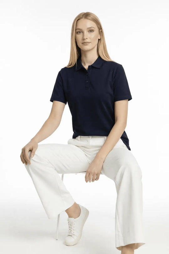 Woman wearing a navy polo shirt and white pants sitting on a white background