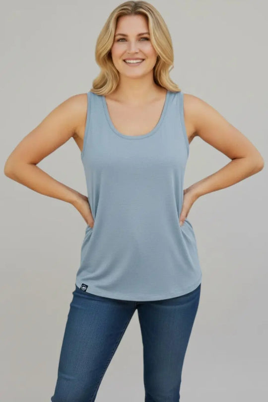 Woman wearing a light blue tank top and dark blue jeans against a gray background