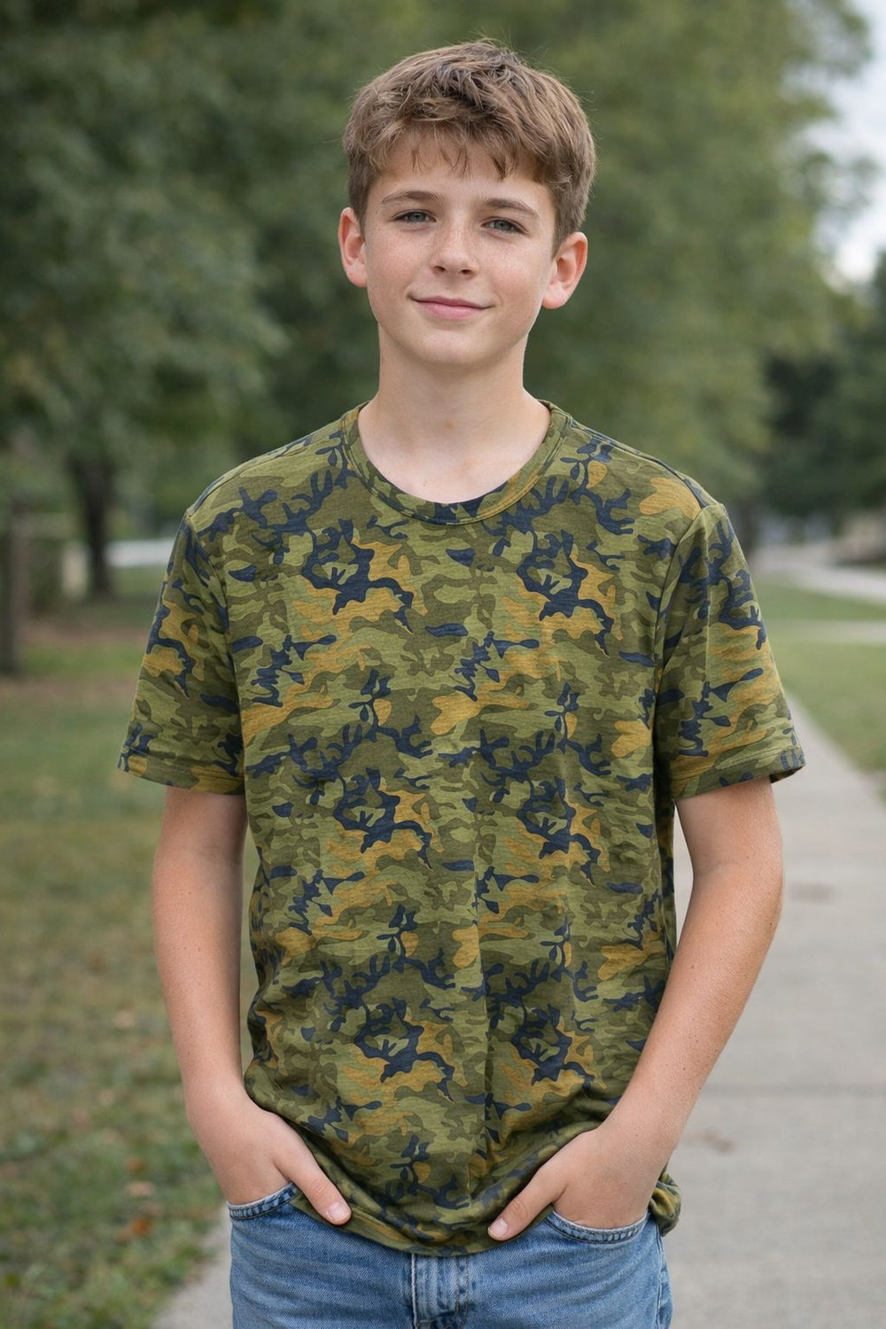 Young boy wearing a camouflage t-shirt standing outdoors with trees in the background