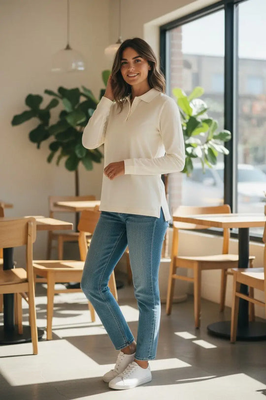 Woman standing in a modern cafe wearing a white blouse and blue jeans.
